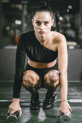 Fototapeta premium Slender Young Woman Doing exercises with dumbbells on the background of the gym
