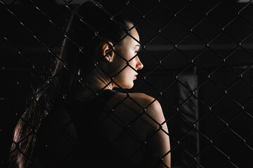 Young woman in a tracksuit in a sparring cage in the gym. Back view