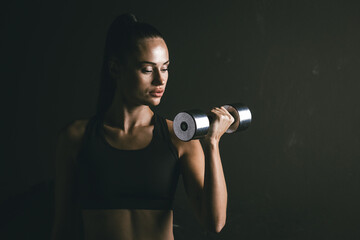 Fototapeta na wymiar Portrait of a woman athlete on a black background with a dumbbell in her hand during exercise. Concept for sports motivation