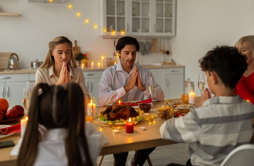 Big multi generation family praying at table before Christmas dinner at home