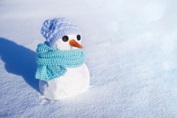 Little cute snowman in a knitted blue hat and scarf on snow on a sunny winter day. Christmas card	