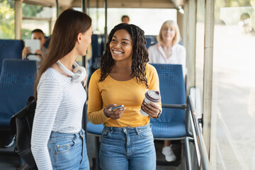 Beautiful multiethnic smiling women standing in bus and talking