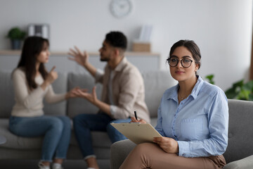 Marriage therapy. Serious family counselor looking at camera while young spouses emotionally arguing, selective focus