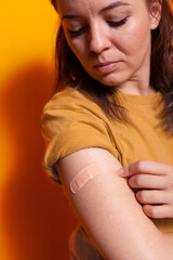 Close up of young woman looking at adhesive bandaid on arm, after receiving vaccine against coronavirus. Person having medical bandage on hand for protection. Vaccinated adult with patch