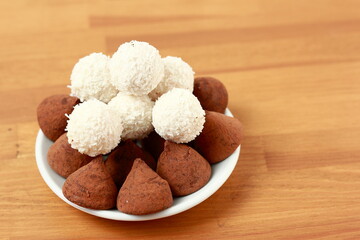 Chocolates made from dark chocolate. White round coconut flakes on the table.