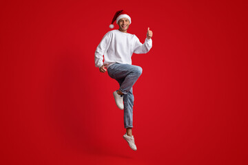 Holiday Deals. Cheerful Man In Santa Hat Jumping And Showing Thumbs Up