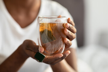 Unrecognizable black lady in pajams holding mug with tea