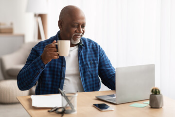African American Senior Businessman Drinking Coffee Using Laptop At Workplace - Powered by Adobe