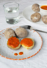 Potatoes on a white plate with red sauce with a glass of water. A traditional Canarian dish is papas arrugadas. Vegetables are boiled in water with a lot of salt. Vertical orientation.