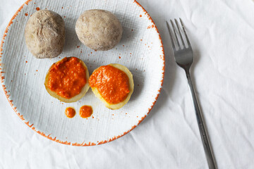 Potatoes on a white plate with red sauce with a fork on a white tablecloth. A traditional Canarian dish is papas arrugadas. Vegetables are boiled in water with a lot of salt. Top view.