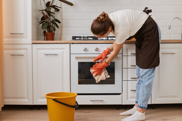 Indoor shot of woman washing steel gas stove and oven. Cleaning the apartment during her day-off,...