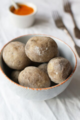 Potatoes on a white plate with red sauce on a white tablecloth. A traditional Canarian dish is papas arrugadas. Vegetables are boiled in water with a lot of salt. Vertical orientation
