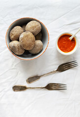 Potatoes in a white bowl with red sauce and wok on a white tablecloth. A traditional Canarian dish is papas arrugadas. Vegetables are boiled in water with a lot of salt. Top view.