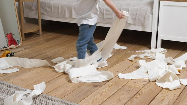 Small child has made a mess, scattered toilet paper around the apartment and happily plays. Little child having fun in the midst of chaos