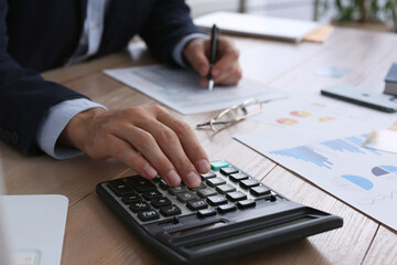 Tax accountant with calculator working at wooden table, closeup