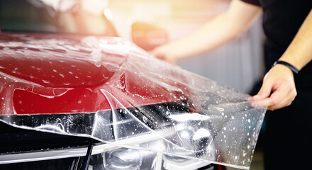 Process of pasting hood of red car with protective vinyl film from gravel chips and scratches. Transparent protection for paint