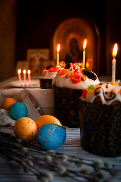 Easter still life with Easter cake, Easter eggs, willow branches and burning candles in the darkness of monastry church with Russian icons in the background