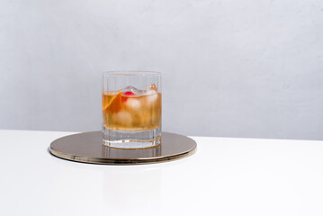 Vaso de vermut con hielo decorado con cerezas y rodajas de naranja sobre mesa blanca	