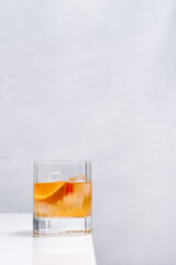 Vaso de vermut con hielo decorado con cerezas y rodajas de naranja sobre mesa blanca	