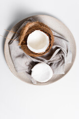Coco abierto con trozos de coco y cáscara en un plato beige sobre un paño de lino. Vista superior	