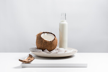 Una botella de leche de coco y un coco abierto sobre una mesa blanca