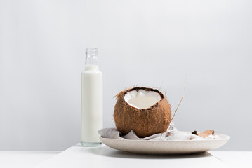 Una botella de leche de coco y un coco abierto sobre una mesa blanca