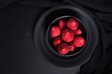 Fresas rojas en una placa negra sobre un fondo negro. Vista superior