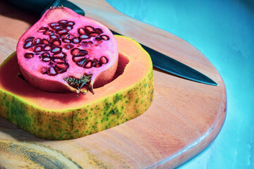 Pomegranate and ripe sliced papaya fruits on wooden chopping board. 