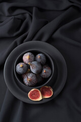Higos negros enteros y cortados en un cuenco negro. Fruta madura sobre fondo oscuro. Vista superior	