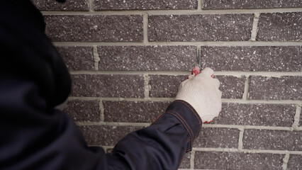 Grouting seams on the facade of the building with a trowel. A worker levels the seams with a trowel on the facade tiles of a house. Alignment of seams with a trowel.