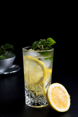 Un vaso de refrescante zumo de limón, cóctel de frutas con rodajas de limón y hielo sobre fondo negro	
