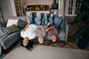 Happy family mom and two sons fooling around and lie upside down on the sofa
