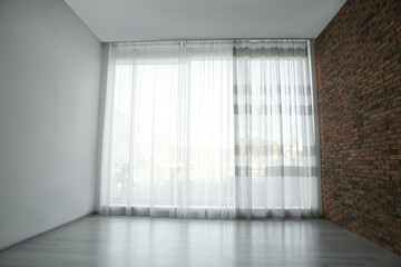 Empty room with red brick wall, large window and wooden floor