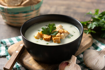 Garlic soup topped with croutons in black bowl on wooden table