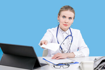 A female doctor sits at a desk on a blue background, writes out a prescription. Hospital. Chief...