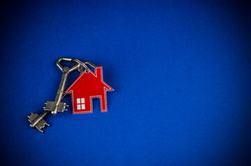 Key and house shaped keychain arrangement on blue background. Top view, flat lay. Real estate, insurance concept, mortgage, buy sell house, realtor concept