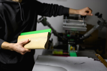 Partial shot of craftsman holding squeegee near screen printing press 