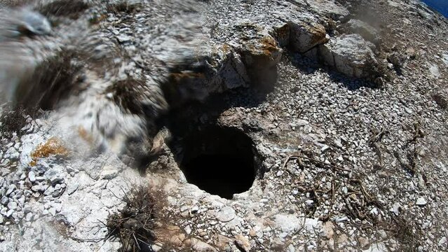 Hole in the ground above a sea cave on the coastline of Vis island, Adriatic Sea, Croatia (Blurry effet from water drops on the lens)
