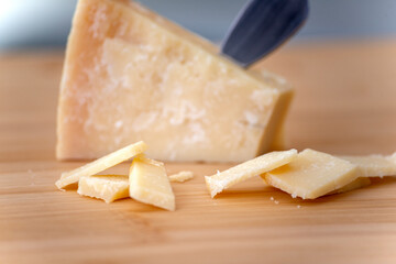 piece of parmesan cheese with slices on wooden cutting board in natural light