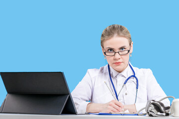 A female doctor sits in glasses, next to a laptop at her desk on a blue background. Therapist....