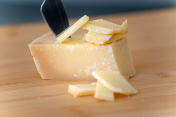 piece of parmesan cheese with slices on wooden cutting board in natural light