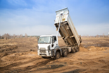 Fototapeta dump truck with a raised body in the process of working on a construction site. transportation and unloading of soil on a construction vehicle. obraz