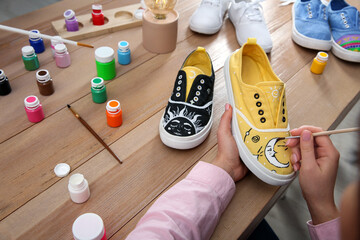 Woman painting on sneaker at wooden table, closeup. Customized shoes