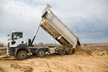 Fototapeta dump truck with a raised body at a construction site in the process of unloading soil. Site preparation for construction, earthworks obraz