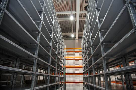 empty gray and high shelves of a large warehouse lit by lamps