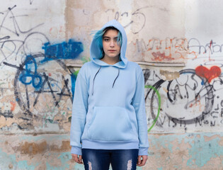 Blue haired Teenage girl in light blue oversize hoodie pointing against graffiti wall