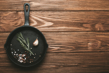 Black cast iron frying pan skillet with food cooking ingredients fresh rosemary, garlic, salt and...