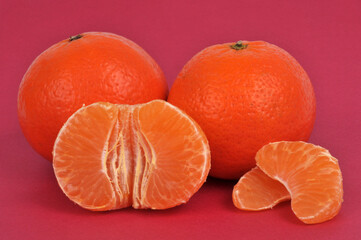 Mandarines entières et mandarine épluchée en gros plan sur fond rouge