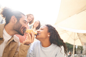 Funny photo of a couple eating a croissant as a joke while friends look on in the background.
