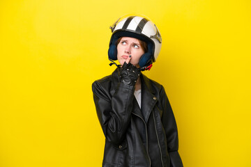 Young English woman with a motorcycle helmet isolated on yellow background having doubts